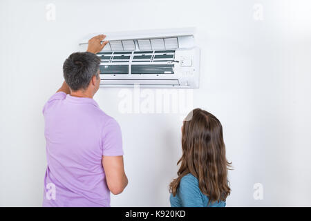 Couple Checking Air Conditioner Attached On White Wall Stock Photo