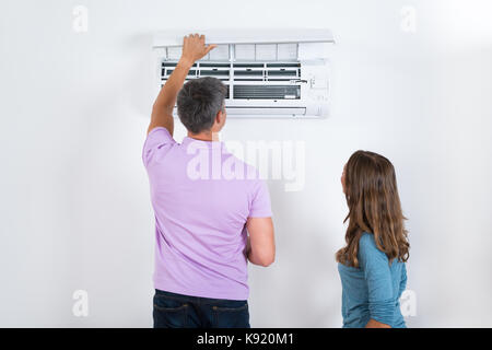Couple Checking Air Conditioner Attached On White Wall Stock Photo
