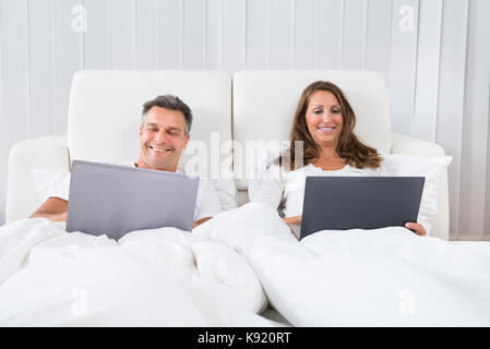 Portrait Of A Happy Couple Using Laptop On Bed Stock Photo
