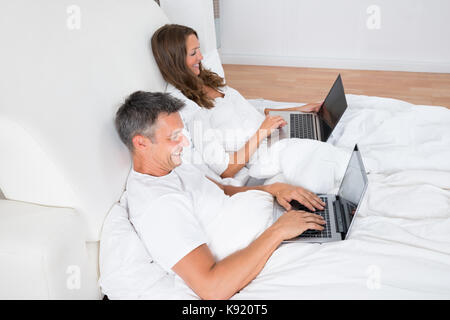 Portrait Of A Happy Couple Using Laptop On Bed Stock Photo