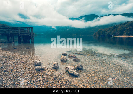 Wooden pier on the lake. Dramatic moody image with rainy clouds above the water surface. Image is taken on lake Bohinj in Slovenia. Stock Photo