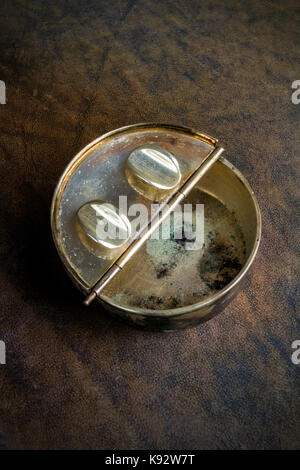 Antique portable metal pocket ashtray on a dark brown leather background Stock Photo
