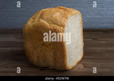 Hand baked and cut loaf of bread on a wooden bench by a grey painted brick wall Stock Photo