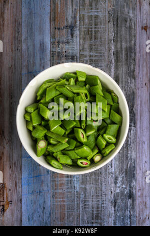 Freshly chopped runner beans in an old white china bowl, on a rough wooden bench