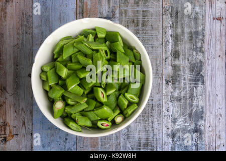Freshly chopped runner beans in an old white china bowl, on a rough wooden bench Stock Photo
