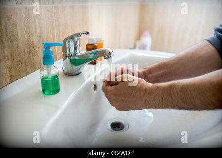 closeup of a young caucasian man washing his hands with soap in the sink of a bathroom Stock Photo