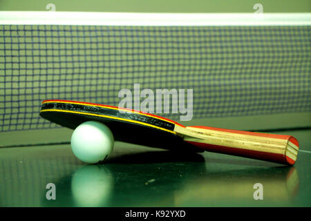 A table tennis or ping pong rackets and ball on a green table with net Stock Photo