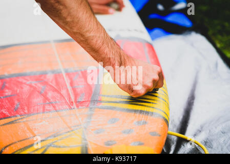 Close up view of hand waxing surf board outdoors. Man is removing or applying wax to surfboard shortboard on vacation. Traces of wax are visable. Stock Photo