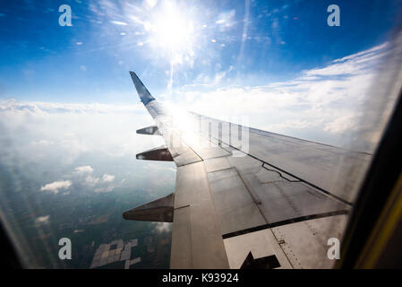 Looking trough window of an aircraft, airplane or plane wing. View from plane window during landing or takeoff over the city urban area. Stock Photo