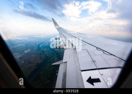 Looking trough window of an aircraft, airplane or plane wing. View from plane window during landing or takeoff over the city urban area. Stock Photo