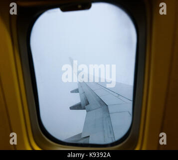 Looking trough window of an aircraft plane wing in fog. View from plane window during landing or takeoff in extreme foggy weather. Flying through clou Stock Photo