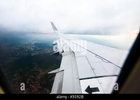 Looking trough window of an aircraft, airplane or plane wing. View from plane window during landing or takeoff over the city urban area. Stock Photo