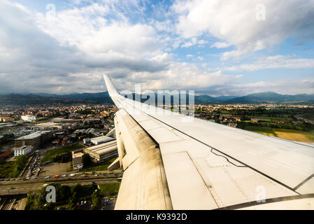 Looking trough window of an aircraft, airplane or plane wing. View from plane window during landing or takeoff over the city urban area. Stock Photo