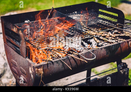 Burning and preheating old rusty barbecue grill cleaning dirty grid. Flames in bbq in nature - outdoors picnic. Preparing the barbecue for charcoal on Stock Photo