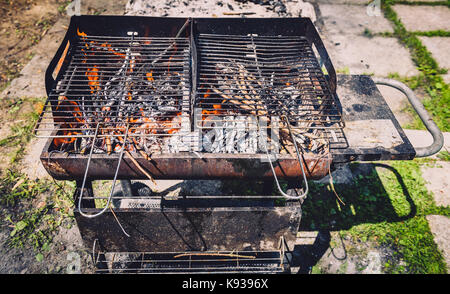 Burning and preheating old rusty barbecue grill cleaning dirty grid. Flames in bbq in nature - outdoors picnic. Preparing the barbecue for charcoal on Stock Photo