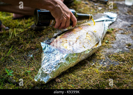 Preparing big dentex fish for barbecue cooking on picnic outside. Salting and wrapping a giant fish in aluminium foil, getting it ready for bbq grilli Stock Photo