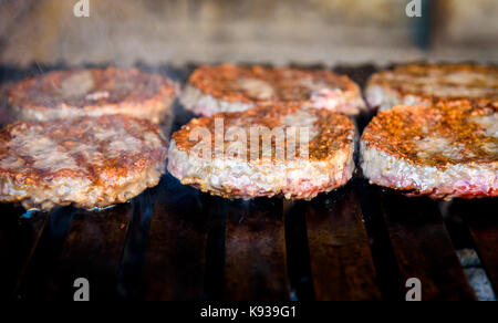 Making and grilling hamburger beef patties on coal grill. Preparing roasted food on barbecue BBQ grill in outdoor fireplace and u-shape fire grid. Stock Photo