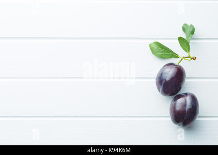 Two fresh plums on white table. Blue plums with leaves. Top view. Stock Photo
