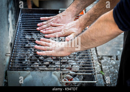 Hands are testing the barbecue heat on charcoal briquettes BBQ. Two people are holding hands over barbecue grill to check and determine the correct te Stock Photo