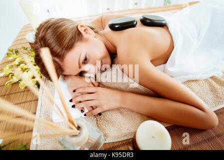 Young beautiful woman relaxing at spa centre. She is enjoying at stone massage. Stock Photo