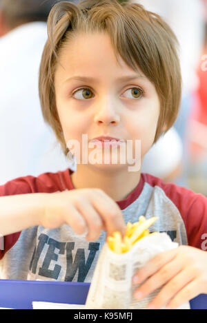 Cute little boy eating fried potatoes at restaurant Stock Photo