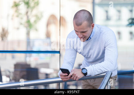 Entrepreneur working texting in a mobile phone leaned on a metal fence with office buildings in the background Stock Photo
