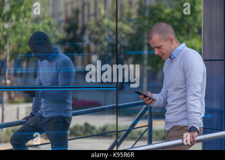 Young handsome businessman standing in front of the building and holding a mobile phone. He goes home from work and uses a cell phone to read new mess Stock Photo