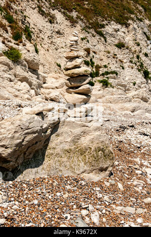 Large weathered rounded rocks placed one on top of another form a stable tapered pillar reflecting summer sunshine stands at the bottom of a cliff Stock Photo