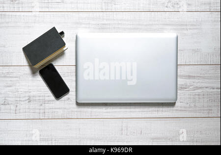 View of a wooden table with a laptop, mobile, notebook and a pen on it Stock Photo