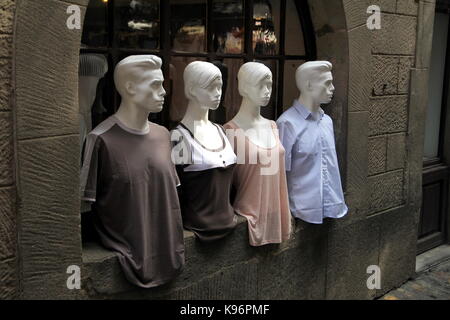 Two male and two female mannequins, dressed in stylish fashion clothes and posed in the window of an old stone building Stock Photo