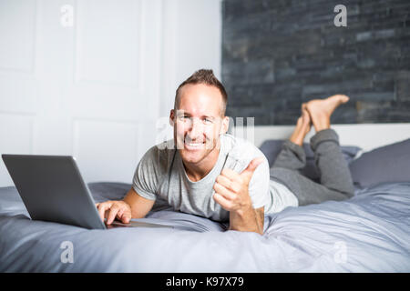 Serious casual young man using laptop in bed at home Stock Photo