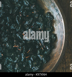 Black dried raisins in plate over wooden background, square crop Stock Photo