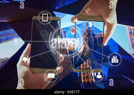 'Fintech' word on digital virtual screen with two businessman hands holding smartphones background. Stock Photo