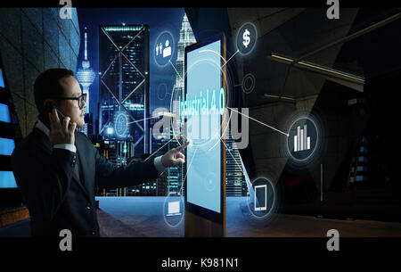 Businessman touching 'Industrial 4.0' word on screen of digital booth with fintech infographic. Hi-tech business concept . Stock Photo