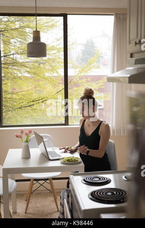 Young woman having breakfast while using laptop at home Stock Photo
