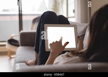 Young woman using digital tablet while lying on sofa at home Stock Photo