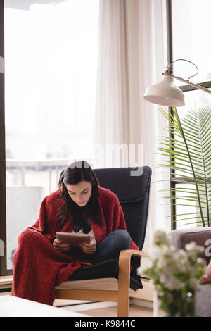 Woman using tablet computer while sitting on chair by window at home Stock Photo