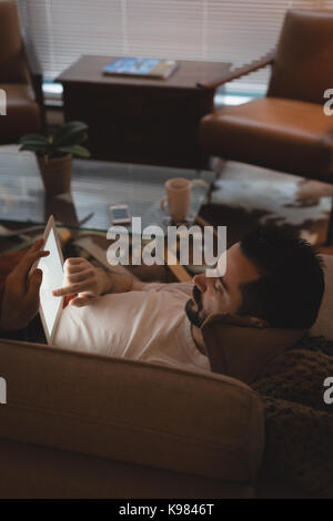 Man using digital tablet while lying on sofa in the living room at home Stock Photo