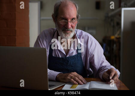 Portrait goldsmith writing in book at workshop Stock Photo