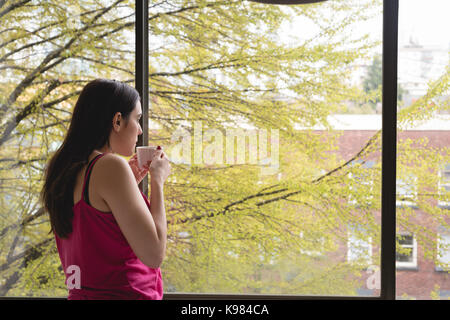 Side view of thoughtful woman with coffee cup standing by window at home Stock Photo