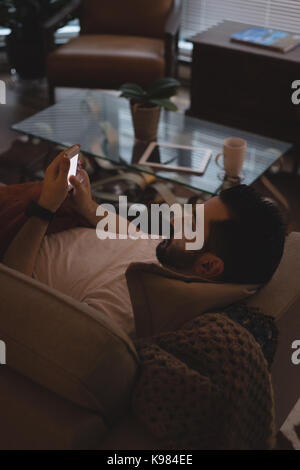 Man using mobile phone while lying on sofa in the living room at home Stock Photo
