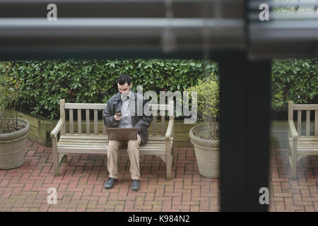 Man using mobile phone while working on laptop in the garden Stock Photo