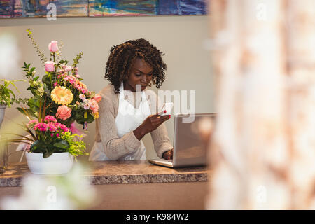 Female florist using laptop and mobile phone in flower shop Stock Photo