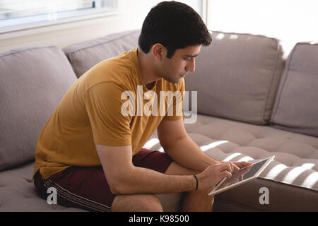 Man using digital tablet on sofa in living room at home Stock Photo