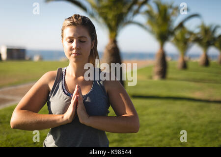 Young woman meditating while standing on grassy field against sky during sunny day Stock Photo