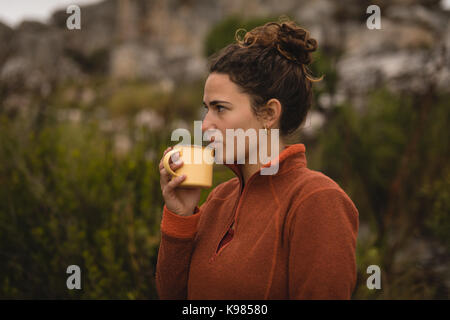Thoughtful woman drinking coffee during mountaineering Stock Photo