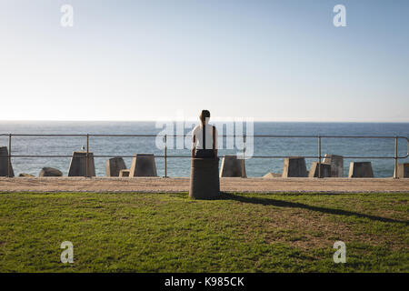 Rear view of young woman standing at beach against sky during sunny day Stock Photo