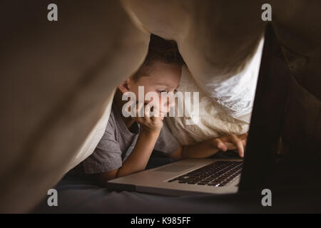 Cute boy using laptop in bedroom Stock Photo