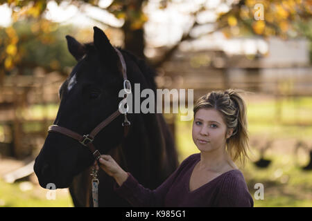 Portrait of young woman with horse standing at barn Stock Photo