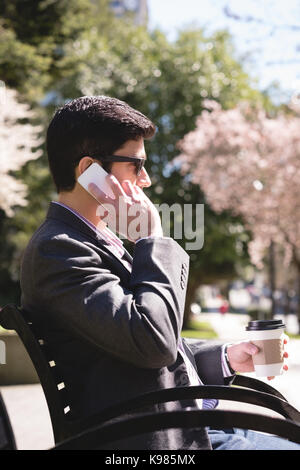 Businessman talking on mobile phone while having coffee in park Stock Photo